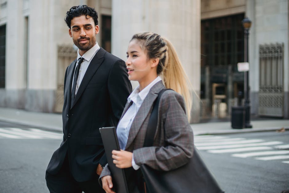 Two business professionals in formal attire walking on a city street, engaged in conversation.